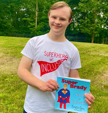 Brady, a blond man with Down syndrome, holds his book, "Super Brady." The cover has a cartoon image of him dressed as a superhero.