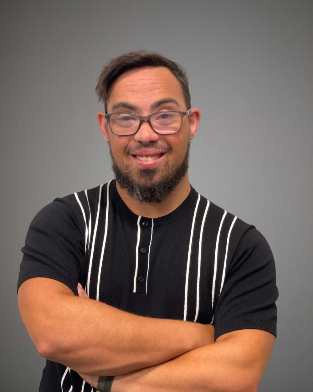 man with down syndrome wearing black shirt with white stripes and smiling with arms crossed